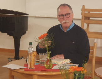 Fritz Blanz mit seinem Buch hinter kleinem Tisch mit Blume und Getränken darauf