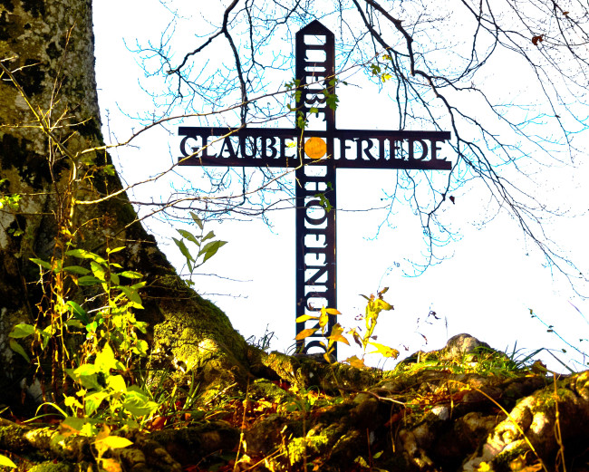 geschmiedetes Kreuz mit Glaube, Liebe, Friede, Hoffnung neben Baum